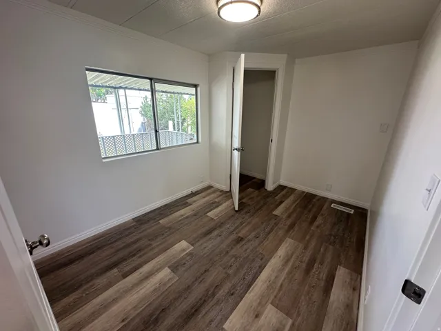 Room featuring wood-finish flooring, white baseboards, a window with metal grilles, and a flush-mount ceiling light fixture