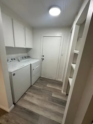 Laundry room featuring wood-finish flooring, white cabinetry, overhead lighting, and built-in shelving