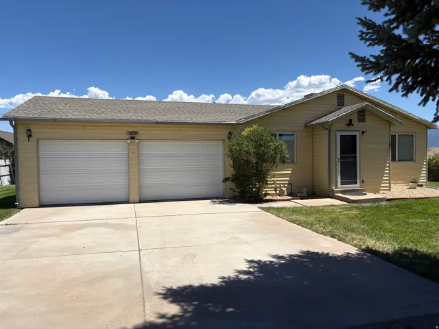 Single-story residence featuring light yellow siding, a two-car garage, a concrete driveway, a front entry with a screen door, and a pitched roof