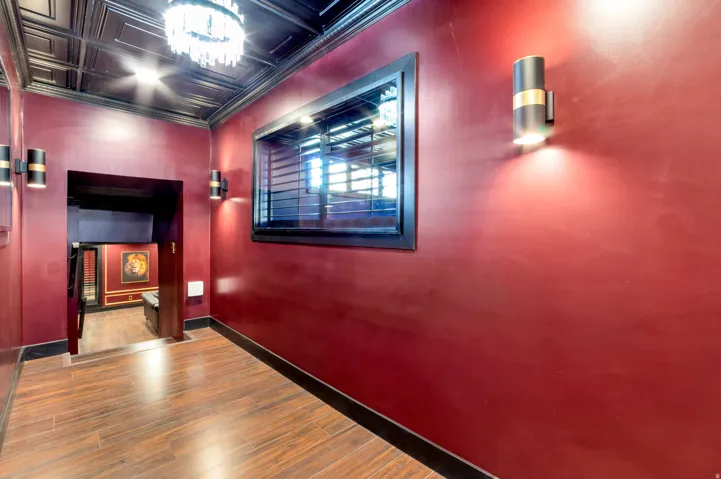 Space featuring rich red walls, wood-finish flooring, a black tin-tile ceiling, a crystal chandelier, and contemporary wall sconces