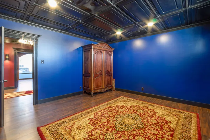 Room featuring wood-finish flooring, a dark pressed tin-style ceiling, blue walls, dark baseboards, and dark door trim