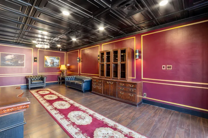 Spacious room featuring dark wood-finish flooring, a black coffered ceiling, and burgundy walls with gold trim detailing