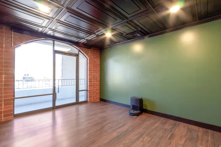 Arch-top glass door with side panels, dark wood-finish flooring, brick wall detailing, green accent wall, and a dark coffered ceiling with recessed lighting