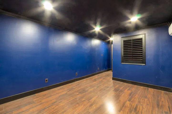 Room featuring wood-finish flooring, dark blue walls, dark ceiling, and black baseboards