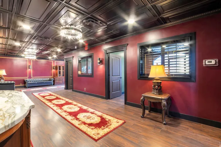 Spacious interior featuring a coffered ceiling, wood-finish flooring, deep red walls, dark trim, and a prominent crystal chandelier