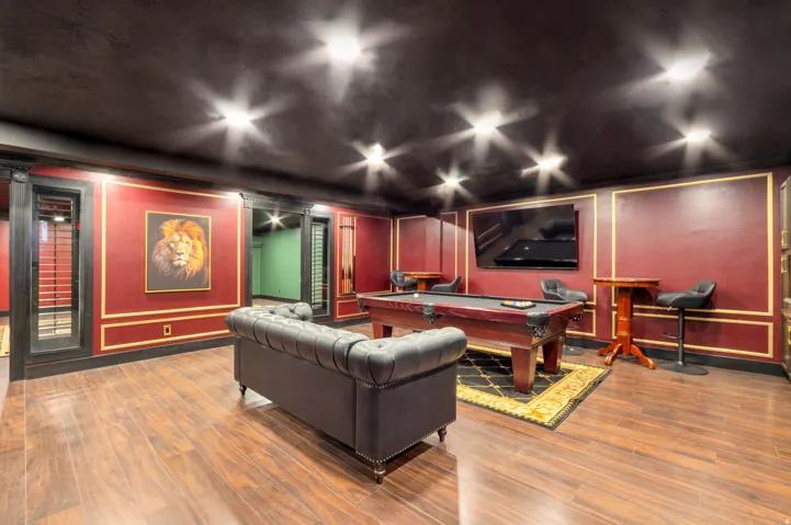 Recreation space featuring wood-finish flooring, a dark ceiling with recessed lighting, and rich red walls with decorative gold trim