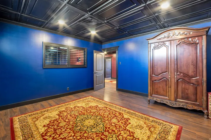 Room featuring rich blue walls, dark wood-finish flooring, and a detailed black tin-panel ceiling with recessed lighting