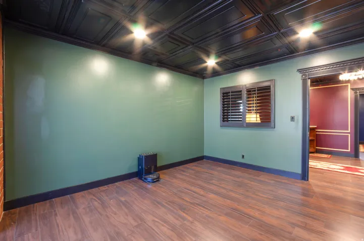 Room with wood-finish flooring, dark green walls, and a pressed tin ceiling