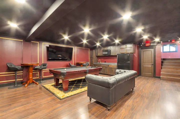 Entertainment room featuring dark wood-finish flooring, a built-in wet bar with cabinetry and sink, recessed ceiling lighting, a mounted television, and a wood paneled door