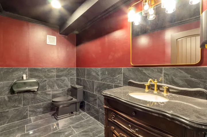 Vanity with a dark stone countertop and brass faucet, complemented by a large framed mirror with brass-toned lighting fixtures