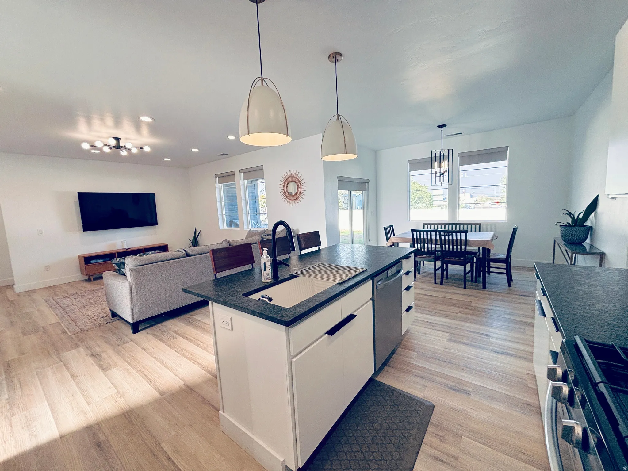 Kitchen island with a dark leathered granite countertop and undermount sink, integrated dishwasher, and pendant lighting