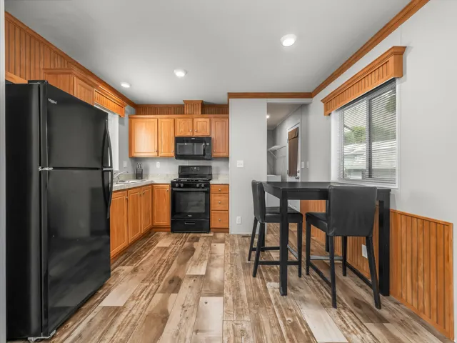 Kitchen featuring wood-finish flooring, recessed lighting, wood cabinetry, stone-finish countertops, and black appliances