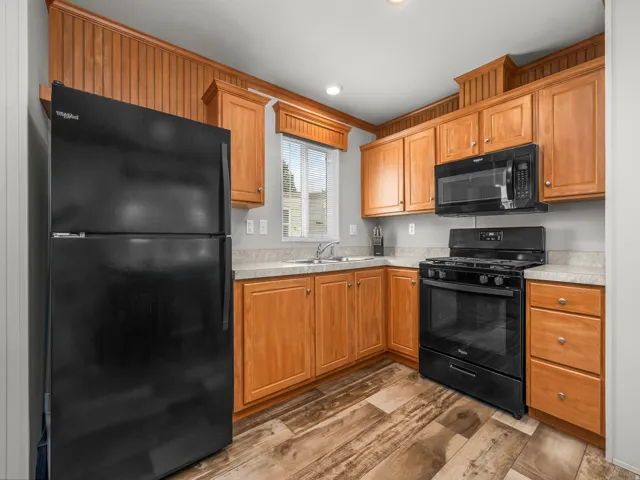 Kitchen featuring wood-finish flooring, wood cabinetry, light countertops, a stainless steel sink, and black appliances