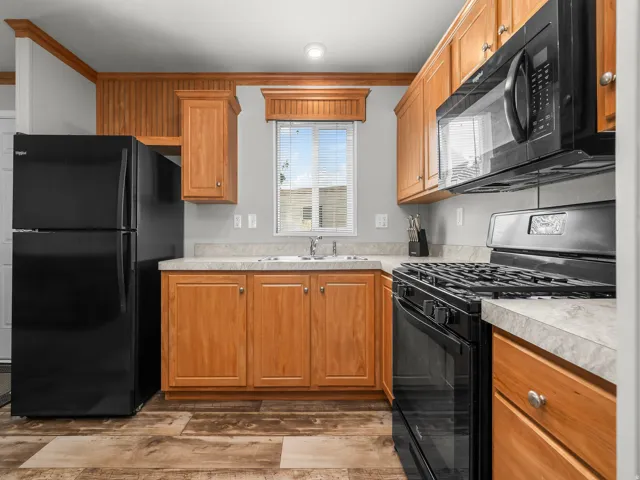 Kitchen featuring wood-finish cabinetry, black appliances, light-toned countertops, and wood-finish flooring