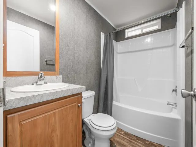 Full bathroom featuring a single vanity with a laminate countertop, wood-finish cabinetry, a white toilet, and a combination tub and shower with an overhead transom window