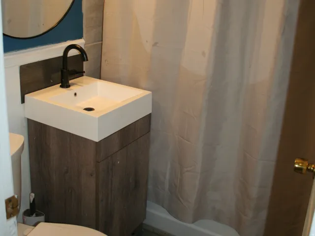 Bathroom featuring a shower area with a white shower curtain, a square basin vanity with wood-finish cabinetry, a round wall-mounted mirror, and a three-light fixture with clear glass shades