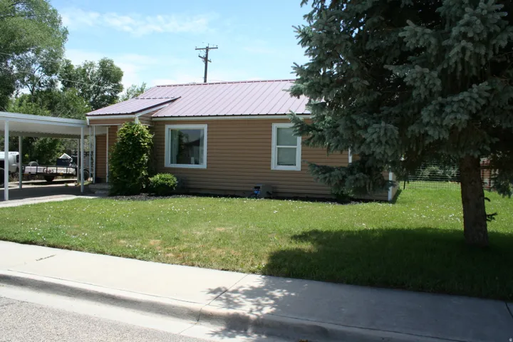 Exterior featuring tan siding, a magenta metal roof, white frame windows, and a covered carport