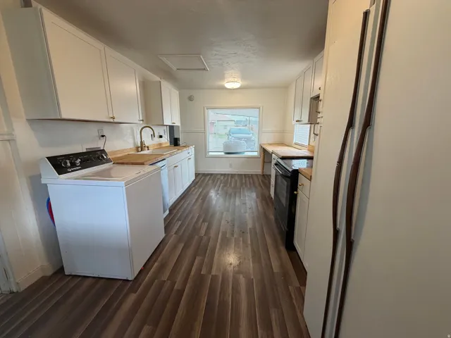 Kitchen area featuring wood-finish flooring, white cabinetry with gold-tone hardware, wood-finish countertops, and a white sink
