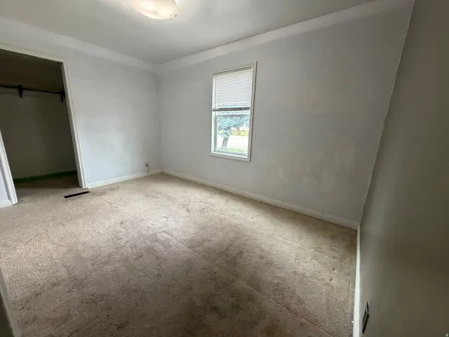 Neutral-toned carpeted room featuring a window with blinds, a flush-mount ceiling light fixture, and a recessed closet space with a clothing rod