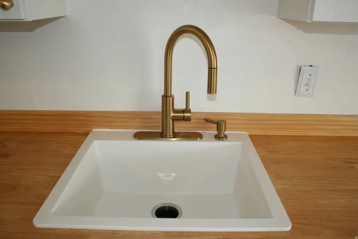 White single-basin sink with a brushed brass pull-down faucet and matching soap dispenser