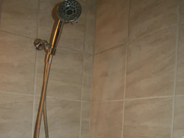 Shower stall featuring square tile walls, a handheld shower head with a flexible hose, and a single-handle shower control