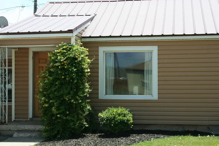Tan horizontal siding exterior featuring a white pane window and a metal roof