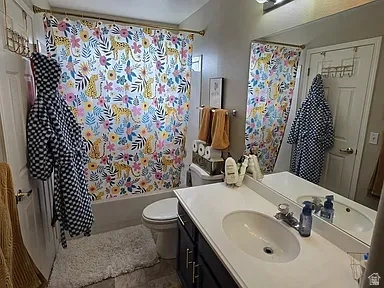 Bathroom featuring a single vanity with an integrated sink, a large wall-mounted mirror, a toilet, a bathtub with a shower, and tile flooring