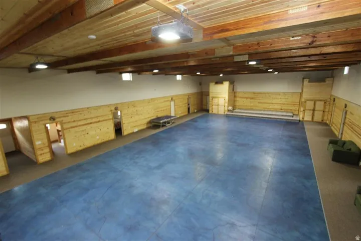 Spacious room featuring a blue flooring surface, wood-paneled walls, and an exposed beam wood-finish ceiling