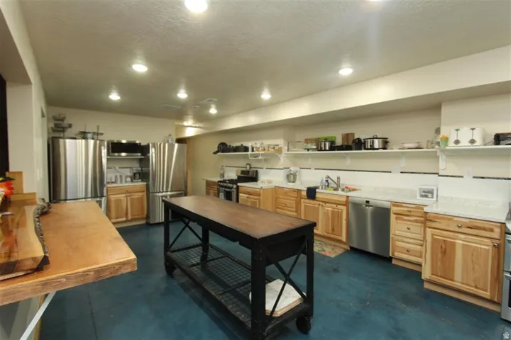 Kitchen featuring stainless steel appliances, light wood-finish cabinetry, light-colored countertops, and open shelving