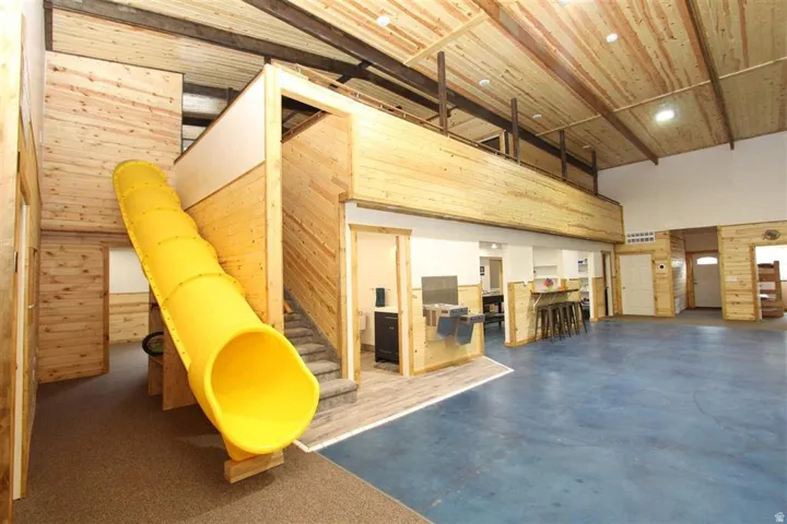 Expansive interior featuring a prominent yellow tube slide, vaulted wood-plank ceilings with exposed beams, wood-paneled walls, a second-story loft, and polished concrete flooring