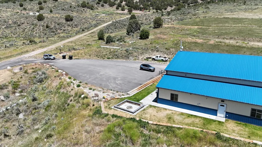 Spacious property featuring a blue metal roof structure, a dedicated parking area, and a stone-lined fire pit