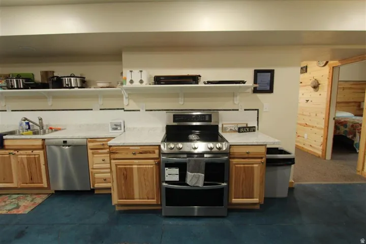 Kitchen area featuring stainless steel appliances, light wood-finish cabinetry, light-colored countertops, and open shelving