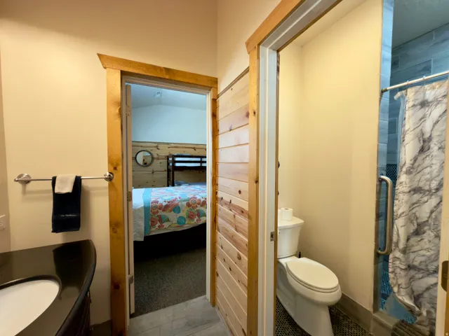 Bathroom featuring a dark countertop vanity with an undermount sink, a toilet, and a walk-in shower with blue subway tile and a grab bar