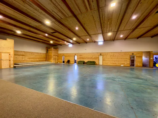 Expansive open-plan interior featuring a high wood-finish ceiling with exposed beams, recessed lighting, wood-paneled walls, and a large stage area