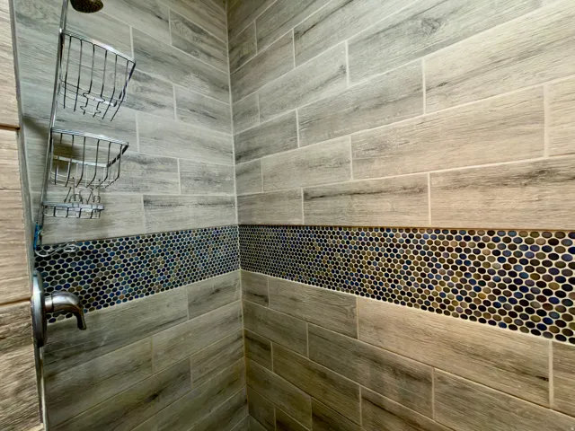 Shower stall featuring wood-finish tile walls with a decorative mosaic tile accent band