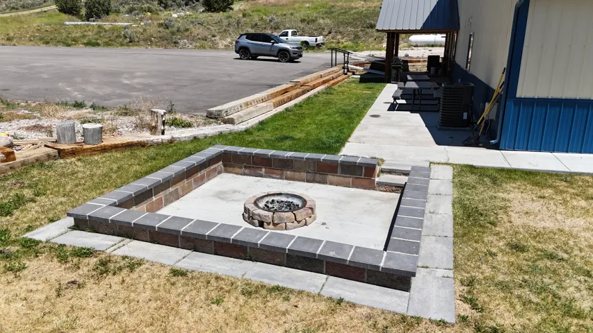 Rectangular stone fire pit with a central stone fire ring, bordered by a concrete patio