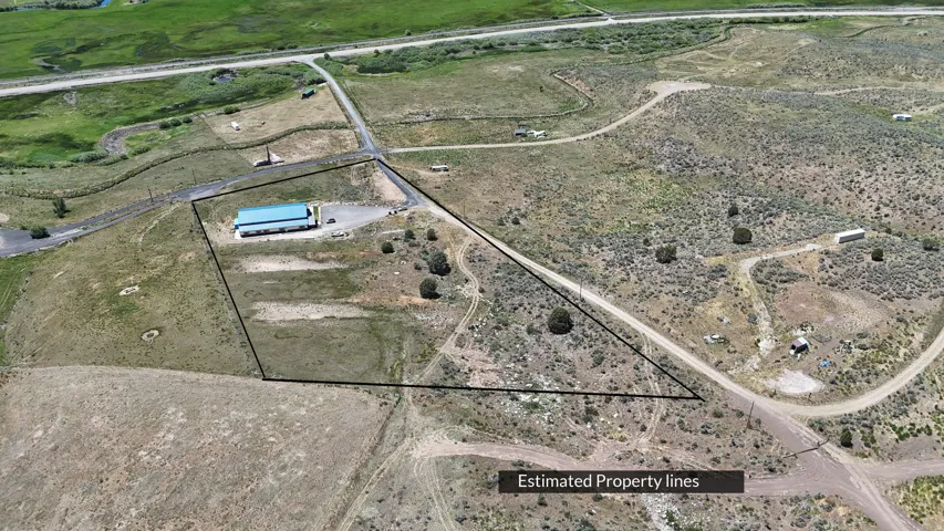 Expansive lot featuring a large building with a blue metal roof, surrounding gravel areas, and direct access to a paved road