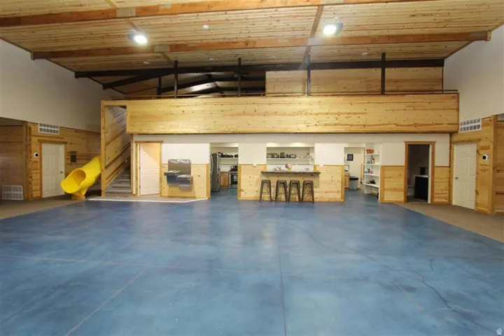 Spacious multi-purpose room featuring a blue-toned floor, a full-height wood-paneled ceiling, and exposed beams