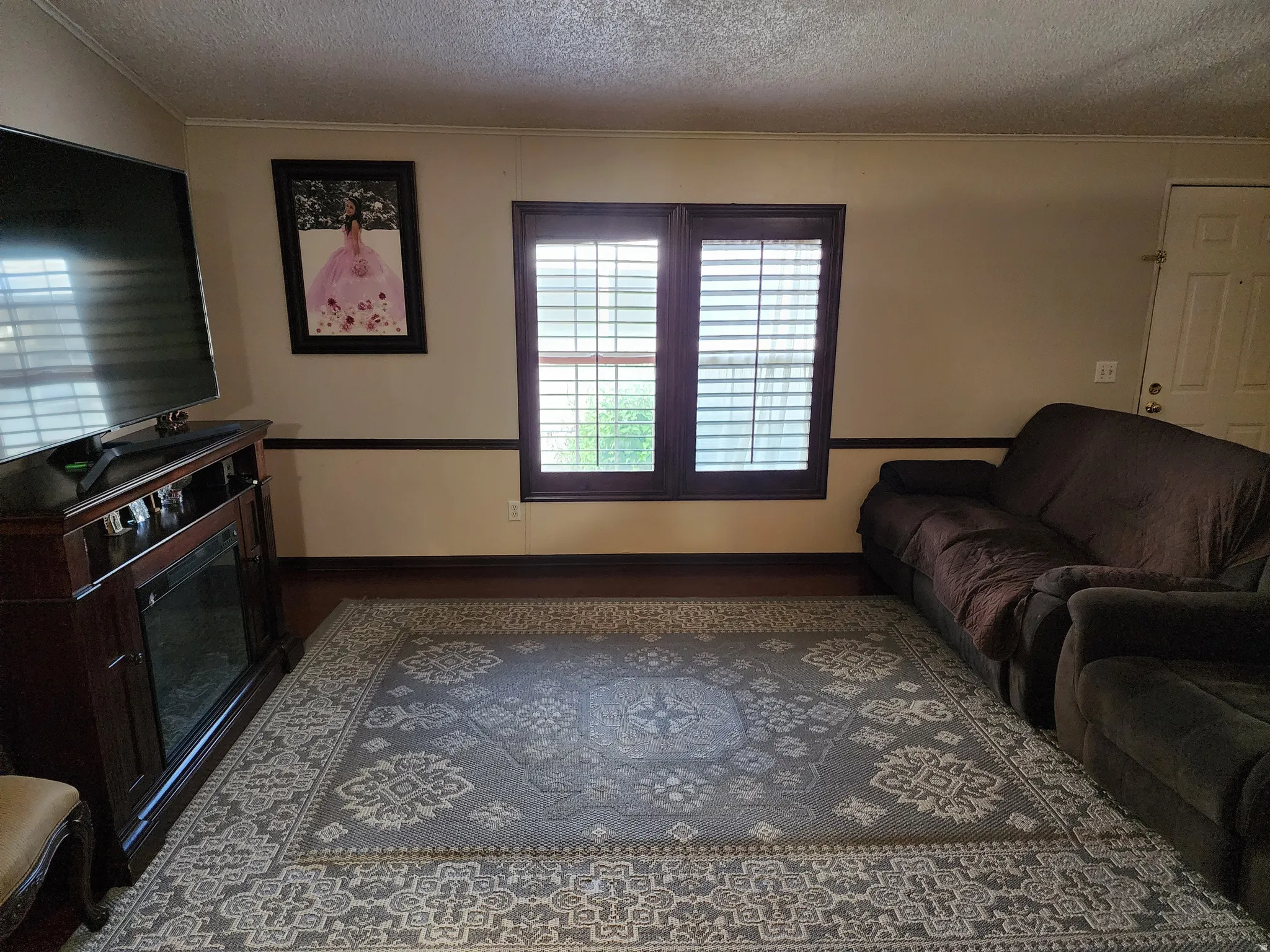 Living area featuring wood-finish flooring, a decorative chair rail, and a window with plantation shutters