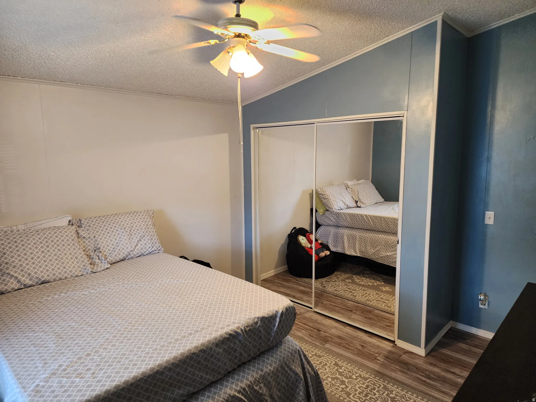 Bedroom featuring a ceiling fan with integrated lighting, wood-finish flooring, and mirrored closet doors