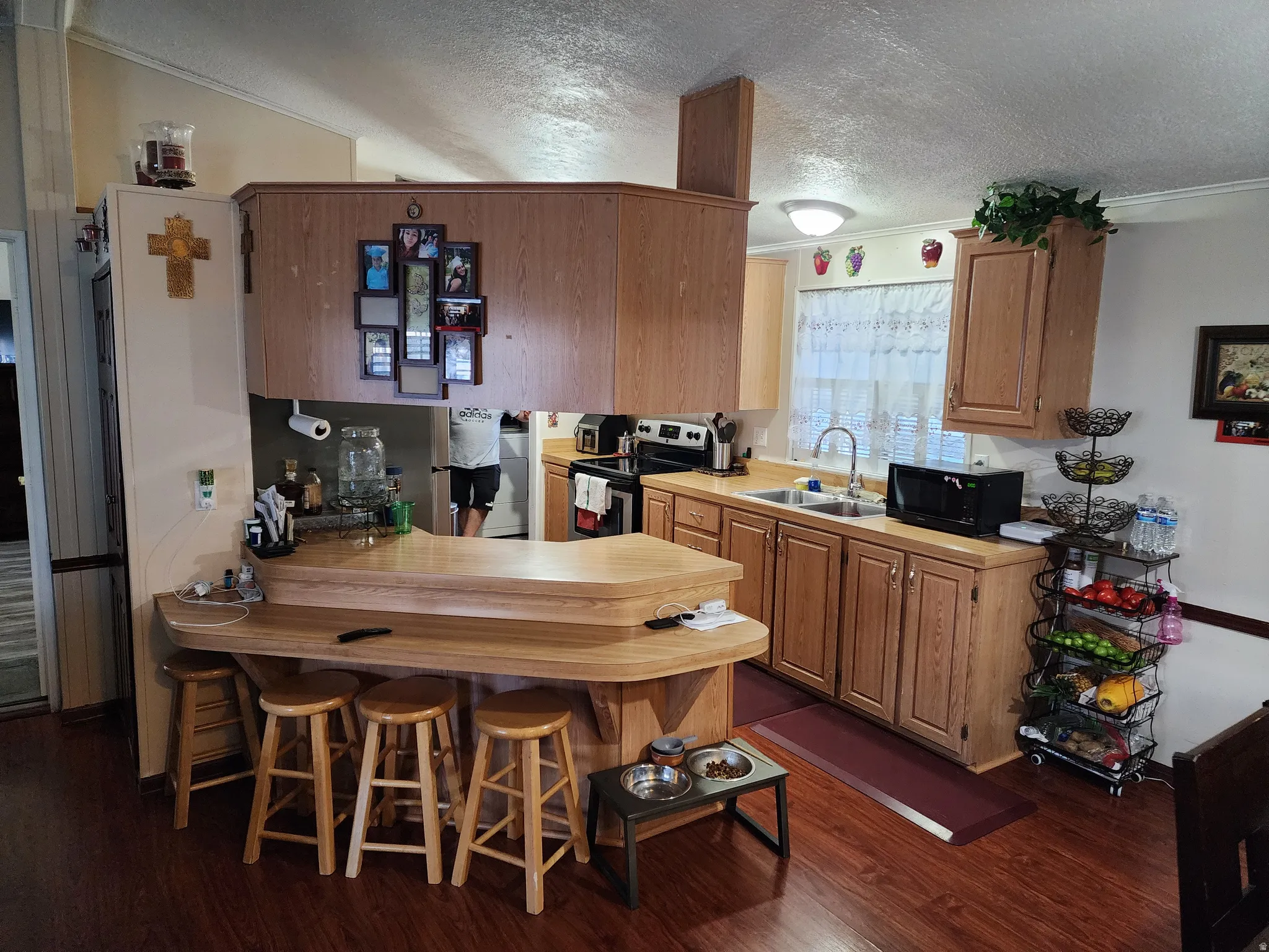 Kitchen featuring wood-finish flooring, a breakfast bar with seating, light wood cabinetry, laminate countertops, and a stainless steel sink with a gooseneck faucet
