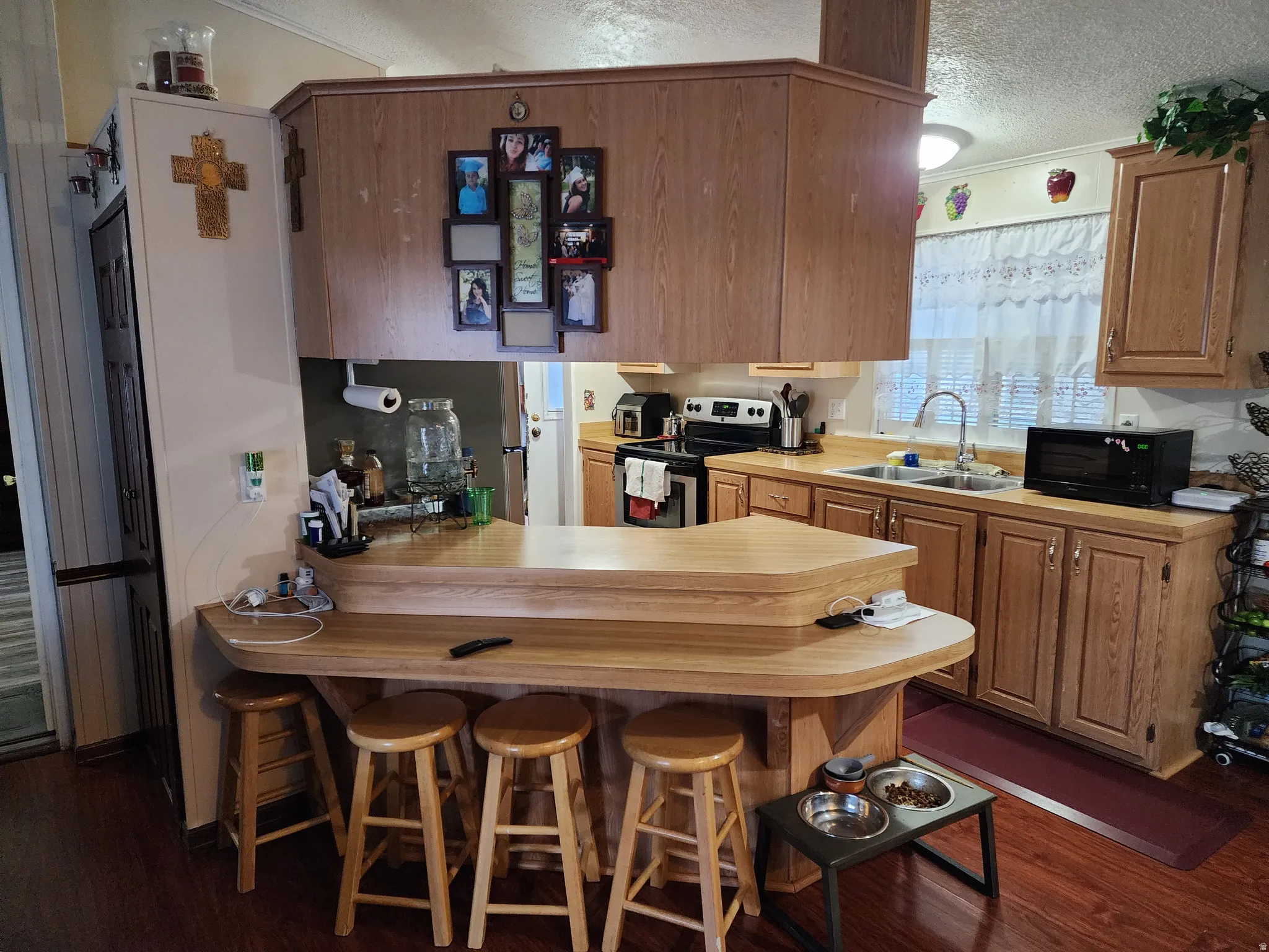 Kitchen featuring wood-finish flooring, a two-tiered breakfast bar, oak cabinetry, a double basin sink, and a window with privacy blinds