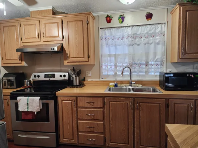 Kitchen featuring wood-finish cabinetry, a stainless steel electric range with an overhead vent, a double basin stainless steel sink with a gooseneck faucet, light wood-finish countertops, and a window with blinds