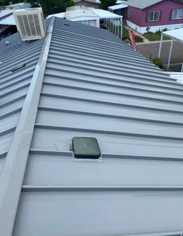 Gray corrugated metal roofing with a ridge vent and a visible swamp cooler unit