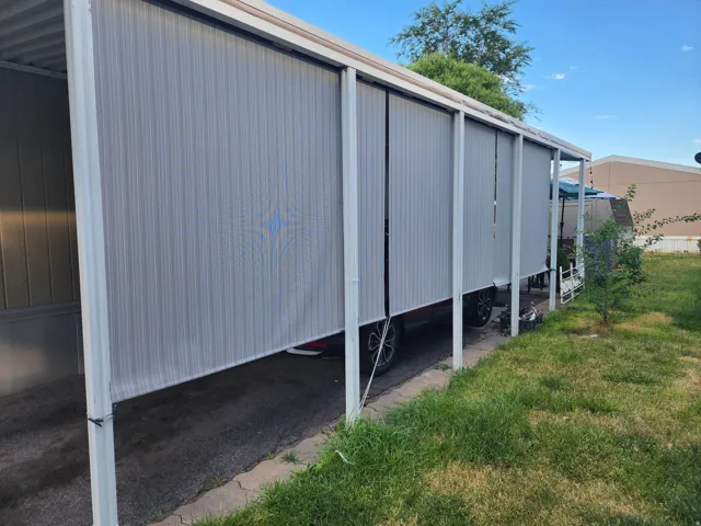 Carport structure featuring a corrugated roof, multiple vertical support beams, and retractable privacy screens