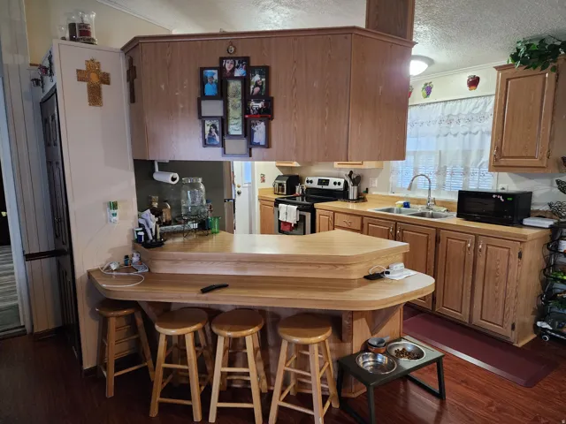 Kitchen featuring wood-finish flooring, a two-tiered breakfast bar, oak cabinetry, a double basin sink, and a window with privacy blinds
