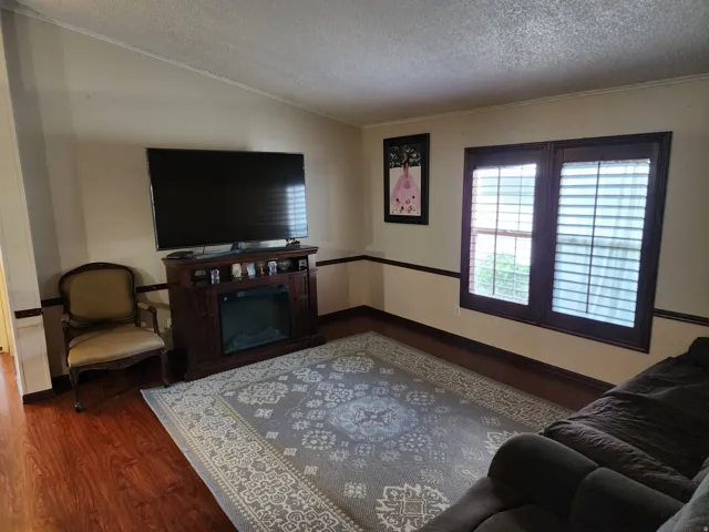 Living area featuring wood-finish flooring, an electric fireplace unit, and shuttered windows