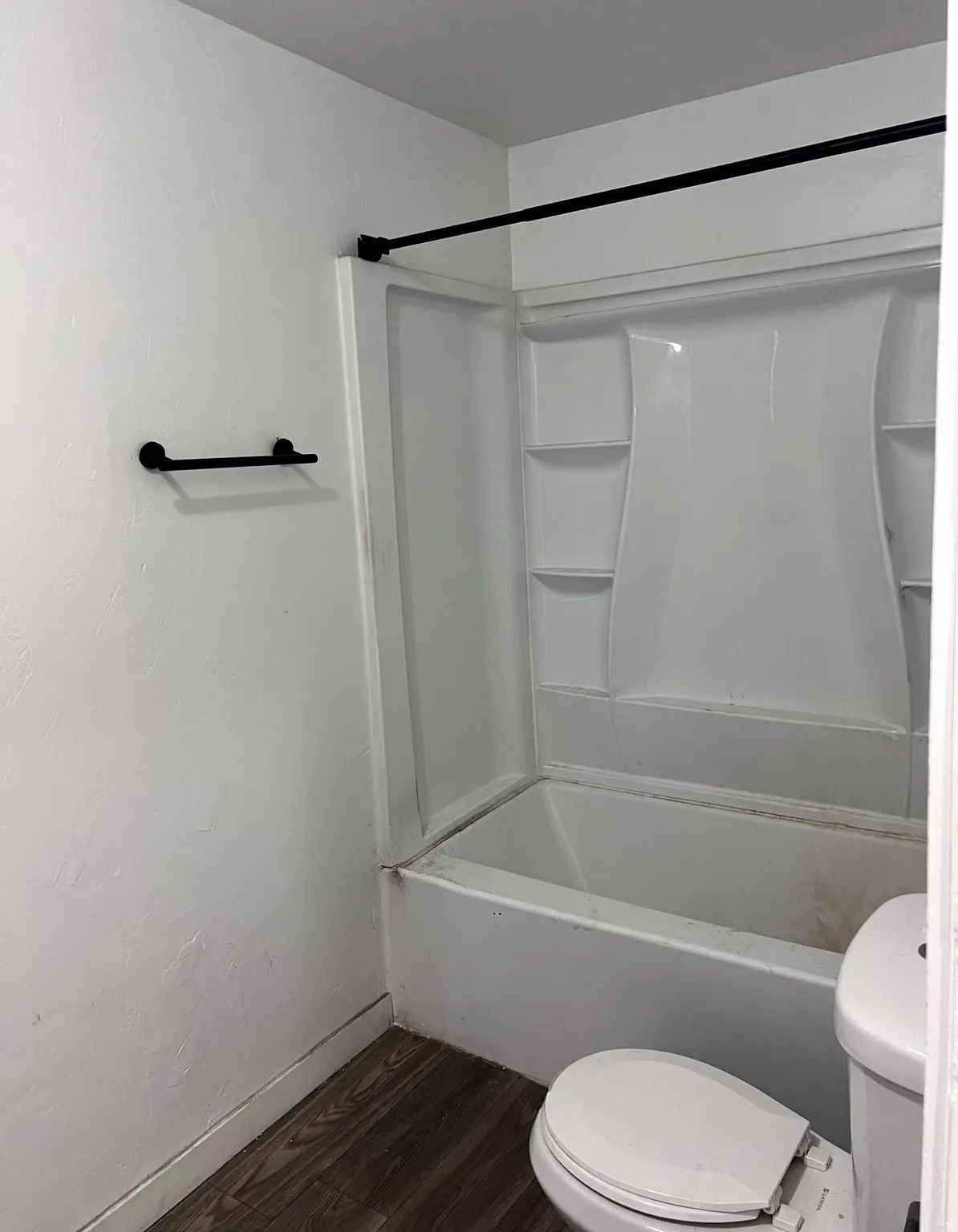 Bathroom featuring a white tub-shower combination unit, matte black shower rod, matte black towel bar, and wood-finish flooring