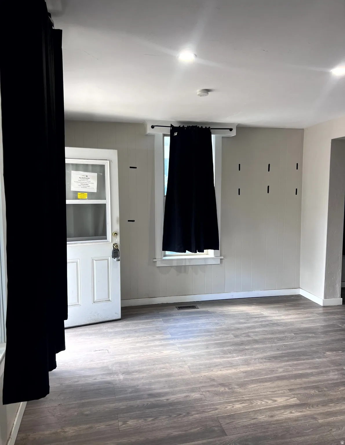 Spacious room featuring wood-finish flooring, recessed lighting, and a white paneled entry door with a storm door