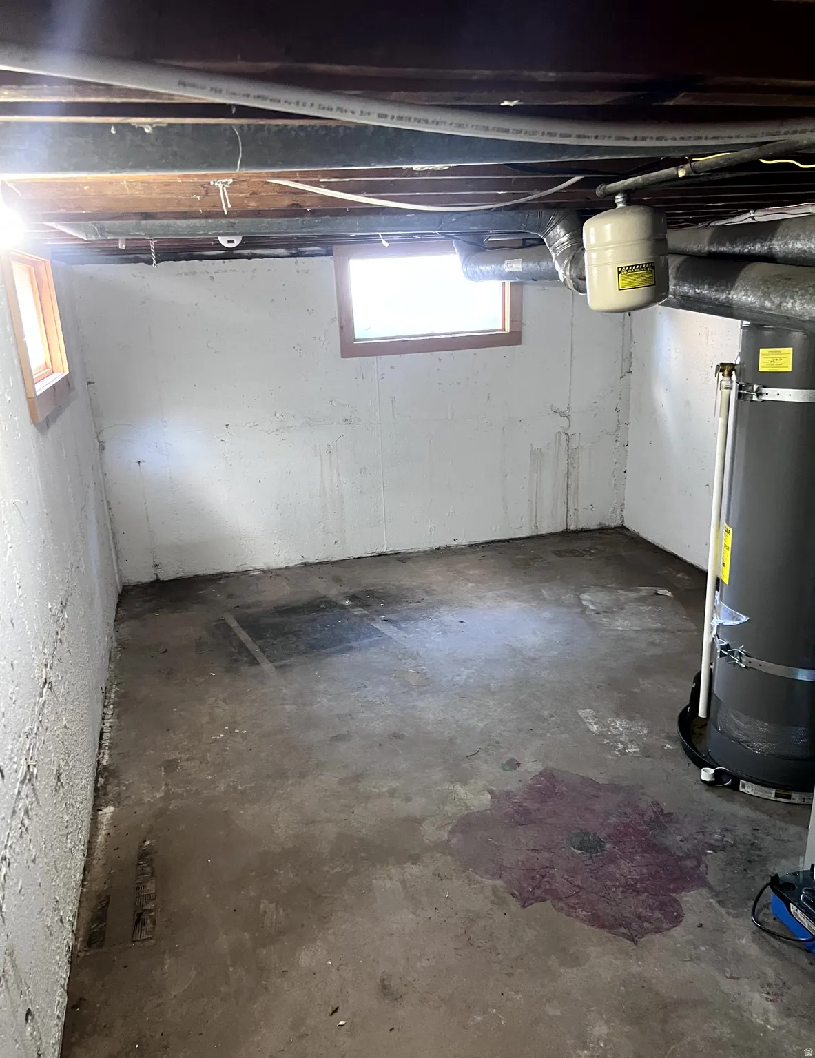 Unfinished basement space featuring concrete walls, exposed ceiling joists, and two small windows